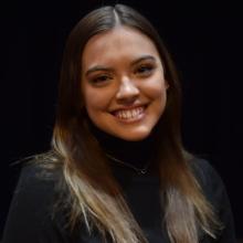 A woman smiling at the camera in front of black background