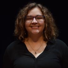 A woman smiling at the camera in front of black background