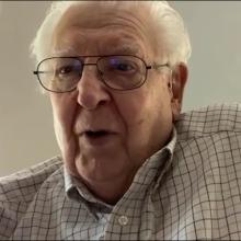 Picture of older man looking at the camera with white wall in the background