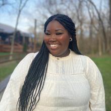 Woman smiling away from camera with trees and grass in the background