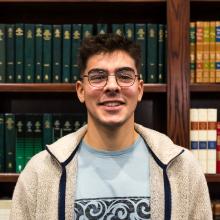 A man smiling at the camera in front of bookshelves.