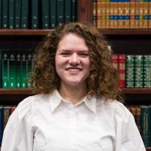 A woman smiling at the camera in front of bookshelves.