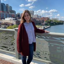 A woman smiling at the camera outside in front of cityscape