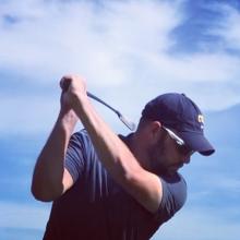 A man swinging golf club with a blue sky 