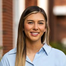 A woman smiling at the camera in front of a brick building.