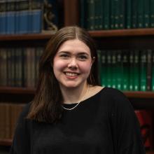 A woman smiling at the camera in front of bookshelves.