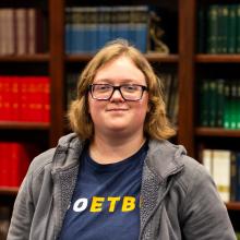 A woman smiling at the camera in front of bookshelves.