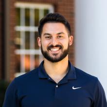 A man smiling at the camera in front of a brick building.