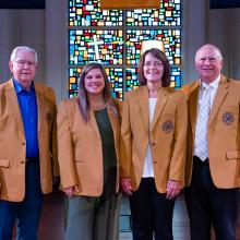2023_homecoming_chapel_0868 Four people in golden-beige blazers standing in front of a stained-glass window.