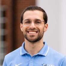 A man smiling at camera in front of a brick building.