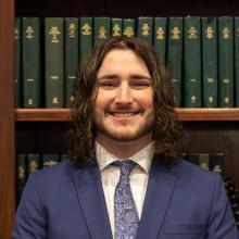 Guy in blue suit in front of a bookcase.