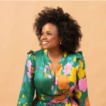 Woman in green floral dress smiling and looking to the left.