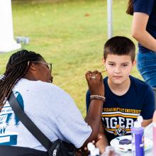 Female student doing facepaint for young boy 