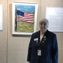 massey Person in a dark blue blazer standing in front of a painting of the American flag.