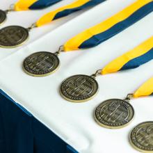 Medals with blue and yellow ribbon laid out on a white table.