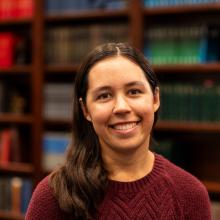 A smiling girl in a red sweater standing infront of a bookcase