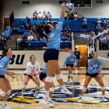 Volleyball player spiking the ball in Ornelas Gym wearing valor blue uniforms.