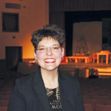 A woman inside in front of a stage in formal attire