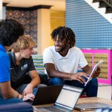 Male students looking at a notebook while sitting in the lobby of a dorm.