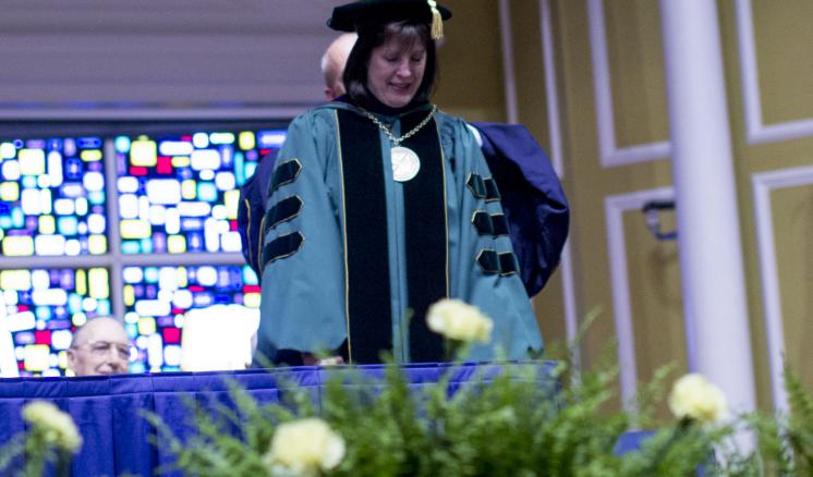 Professor on stage dressed in academic regalia during graduation ceremony
