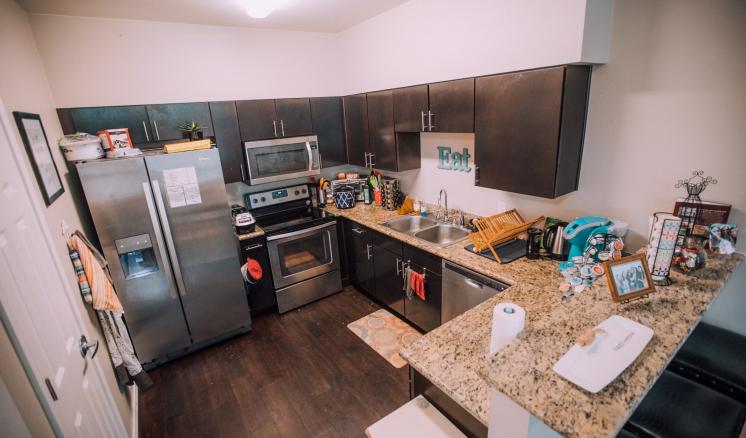 Modern kitchen with dark brown cabinets, light granite countertops, stainless steel appliances, and a small bar area with two stools.