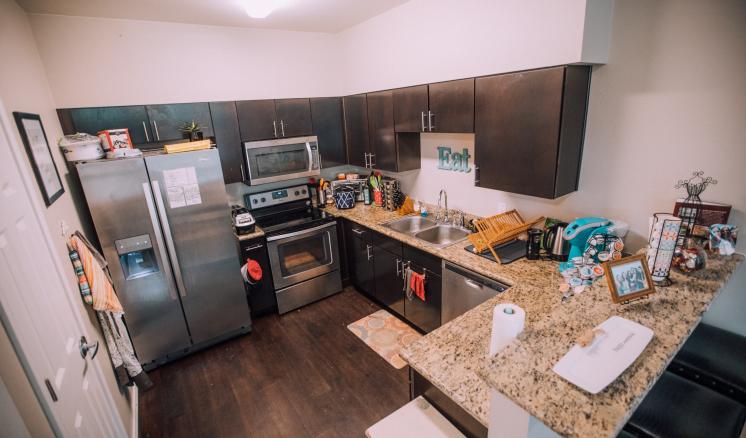 Modern kitchen with dark brown cabinets, light granite countertops, stainless steel appliances, and a small bar area with two stools.