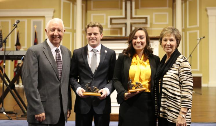 Four people standing together; two in the center hold awards.