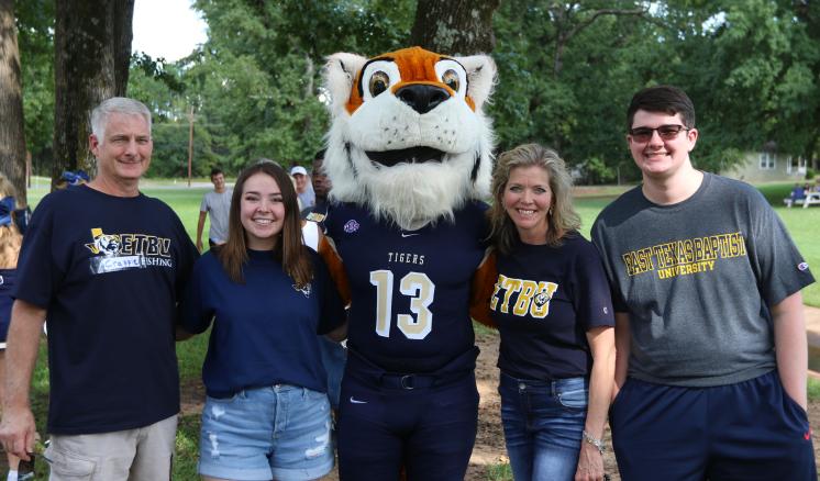 A group of five people stands outdoors with a tiger mascot.