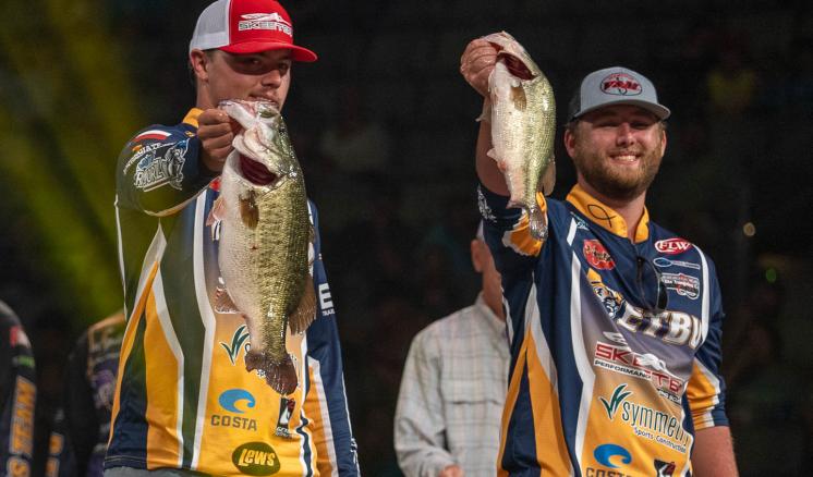 2 men in bass fishing apparrel holding up two largemouth bass