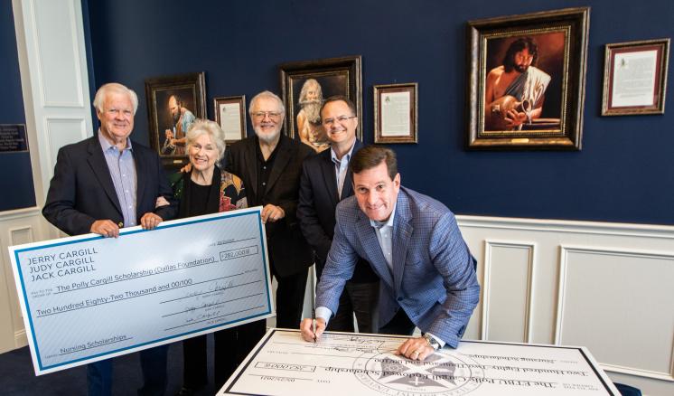 A group of people in formal attire standing around a large check being signed
