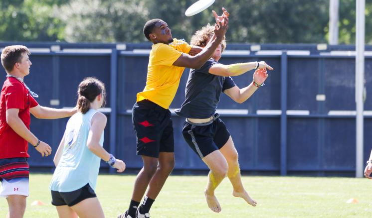 Players leap for a frisbee during an Ultimate Frisbee game on a grassy field.