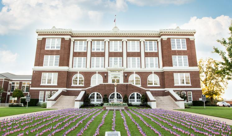 A large brick building with white columns and many small American flags on the lawn.