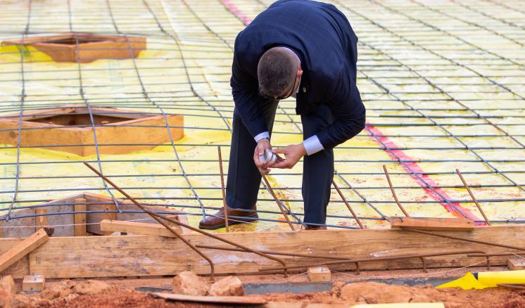 A person in a suit bending over a rebar grid at a construction site.