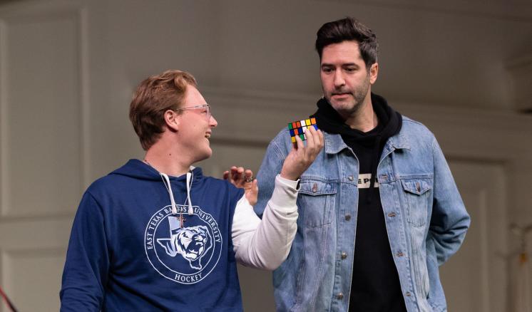 Two people, one holding a Rubik's Cube, standing indoors.