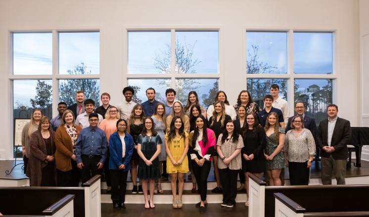 2022_alpha_lambda_delta_honor_society_img_1 A group of men and women smiling at the camera on the stage in a chapel