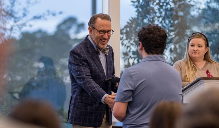 A man shaking hands with another man with big glass windows in the background
