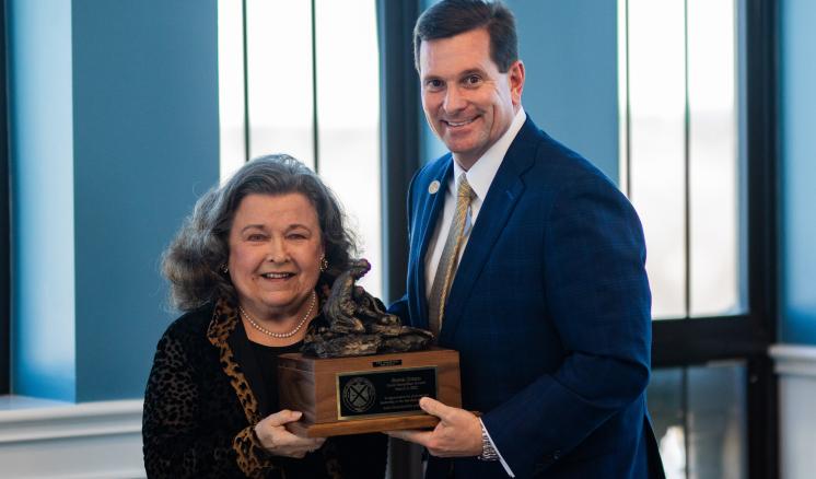 A man and a woman smiling at the camera with an award in between them