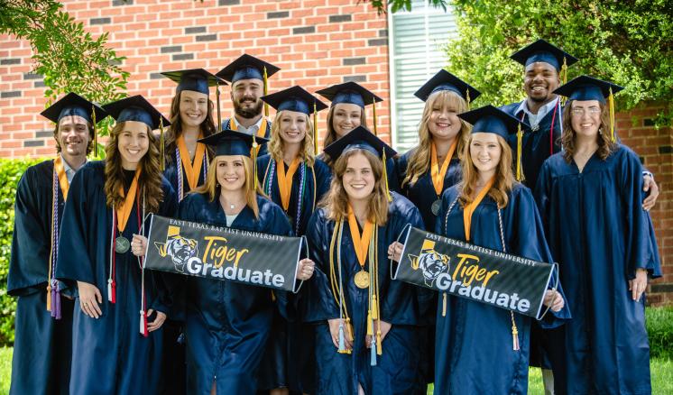 A group of students in graduation regalia holdig Tiger Graduate banners