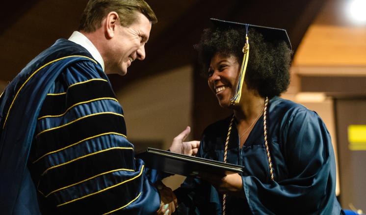 A man and a woman in graduation regalia smiling at each other