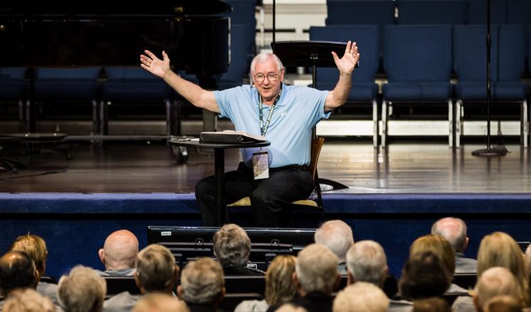 A man speaking with his hands raised in front of an audience