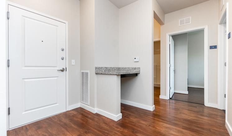 Modern interior space with white walls and dark wood flooring, featuring a closed white door and two open doorways.