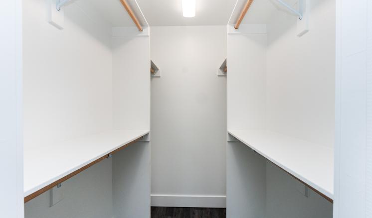 Empty walk-in closet with white walls and dark wooden floor, featuring shelves and hanging rods on each side.