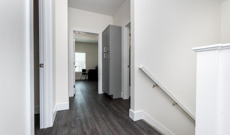 A modern residential hallway with dark flooring, white walls, and a staircase with a white railing.