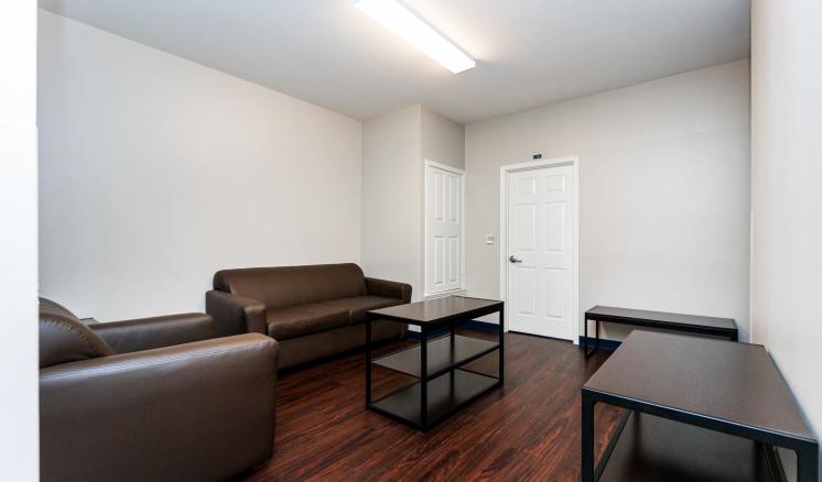 Small room with brown leather couches, wooden floor, and a coffee table.
