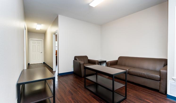 A small living room with a brown leather couch, armchair, and a black coffee table on a wooden floor.