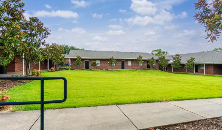 A well-maintained lawn with red brick buildings and a blue sky with clouds.