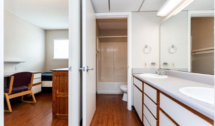 Interior view of a bathroom connected to a small living area with a desk and chair.