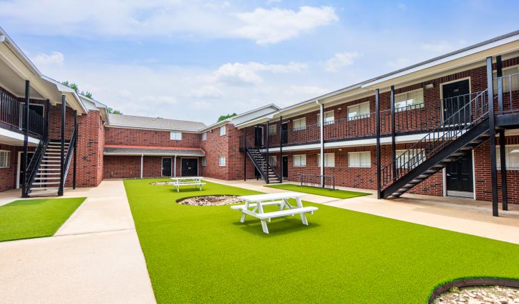 Courtyard of a brick apartment complex with artificial grass and picnic tables.