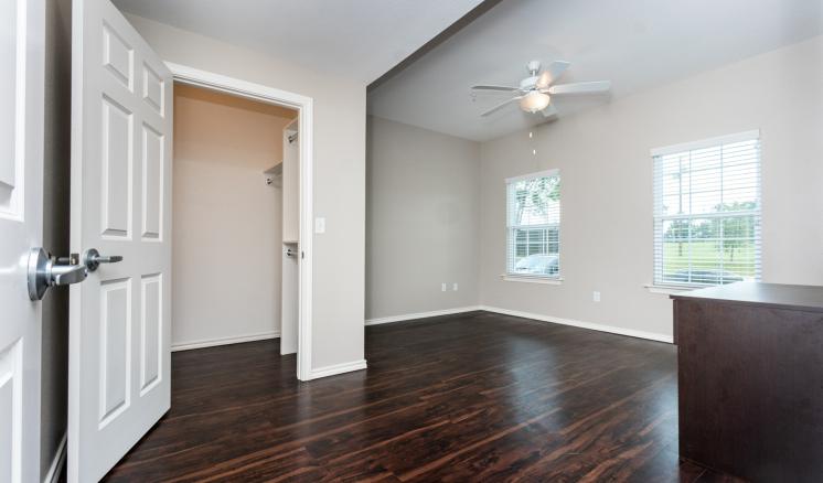 Empty room with dark wood floors, two windows, and a ceiling fan.