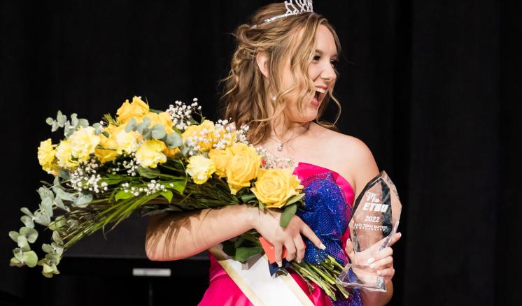 Woman smiling away from the camera with an award and flowers in her hands